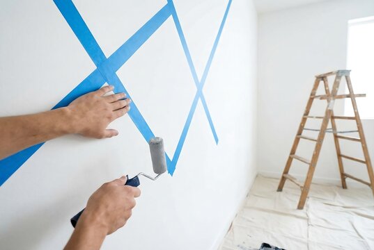 Man creating a geometric pattern on a wall with painters tape and roller. DIY home renovation, interior design and room decoration.