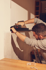 Handyman with battery drill fixing kitchen cabinets and shelf.