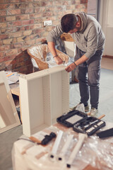 Man working and assembling furniture in a new apartment.