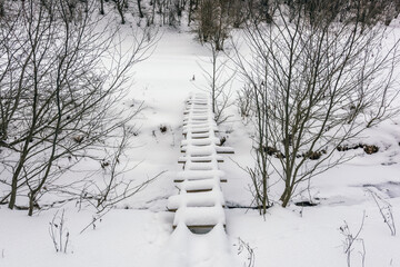 Small Wooden Bridge in Winter Snowy Landscape Over a Stream - Untouched Nature After Snowfall, Aerial View.