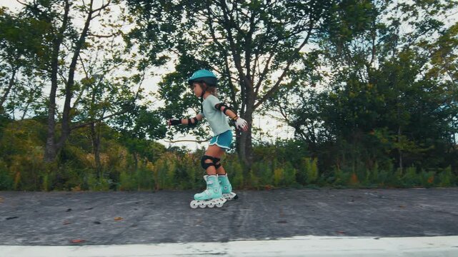 Girl learns roller skating on the road in the park and does her first attempts in the sport