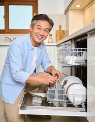 Asian senior man putting dishwasher in the dishwasher at home