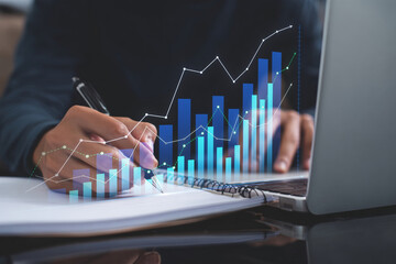 Business professional analyzing financial data and planning strategy with digital growth charts overlayed on a notebook and laptop, symbolizing market analysis, investment, and future development.