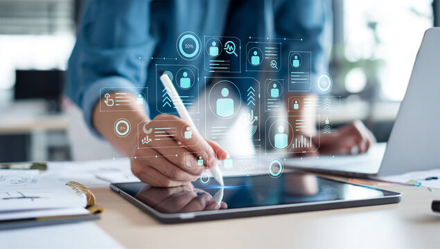 Professional working on a digital tablet with a stylus, interacting with an overlay of data analytics, user profiles, and business intelligence icons - Powered by Adobe