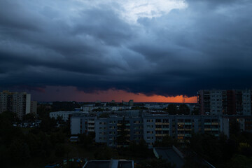 Fototapeta premium View from the window of a city block during an approaching thunderstorm. Heavy clouds and a bright sunset emphasize the sudden change in weather in a residential area.