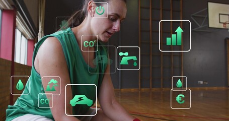 Kneeling mid-adult woman in green sleeveless top tying shoe on parquet gym floor, with green icons