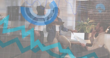 Presenting seated woman in denim holding tablet, gesturing at meeting, with laptop, papers, data