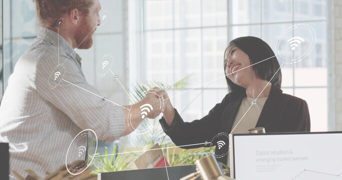 Shaking hands two colleagues in office wearing business attire, with monitor chart and WiFi icons - Powered by Adobe