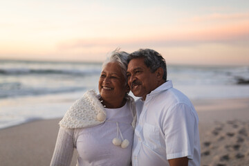 Obraz premium Smiling newlywed senior couple looking away at beach against sky during sunset