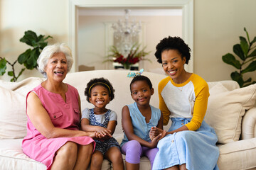 Portrait of african american grandmother, mother and two granddaughters smiling sitting on couch