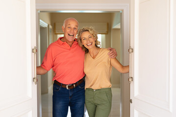 Portrait of caucasian senior couple smiling while opening the front door of house