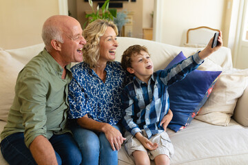 Caucasian grandparents and grandson taking a selfie while sitting together on the couch at home