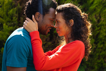 Side view of young multiracial couple romancing while touching forehead in garden