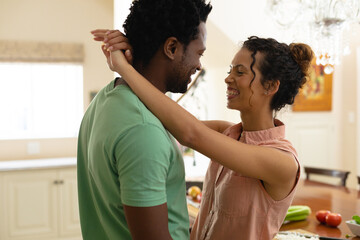 Cheerful young woman romancing african american boyfriend while dancing in kitchen