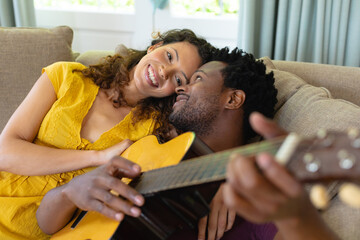 Smiling young couple lying together with guitar on sofa at home