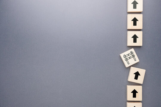Wooden arrow blocks showing upward progress interrupted by a barrier, representing delay, blockage, and obstacle concept