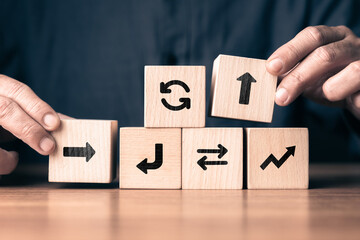 Wooden blocks with arrow symbols arranged by human hands to represent decision making, strategy, and adaptive workflow concept, showing direction changes, planning process