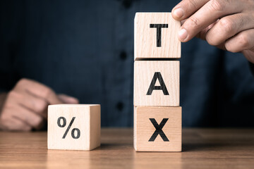 Wooden blocks showing TAX stacked vertically beside a percent symbol, representing tax calculation, financial planning, and cost management concept