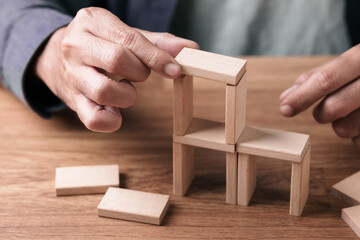 Man arranging wooden blocks to build a stable structure, representing building success through planning, risk management, and strategic decision making