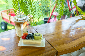 Fresh fruit cream cake topped with strawberry, blueberry, raspberry, and kiwi, served with iced coffee on a wooden table in a cozy cafe setting, bright natural light and relaxing atmosphere