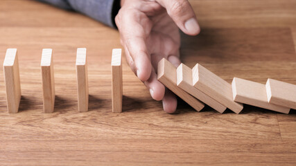 Hand stopping falling wooden blocks like domino to prevent a domino effect, representing risk management, prevention, and control concept for business stability, crisis response