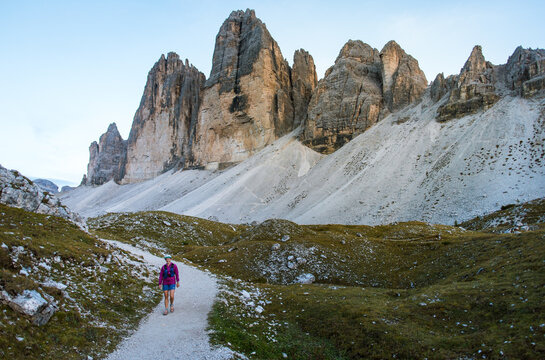 Hiker walks along a scenic mountain trail with dramatic peaks