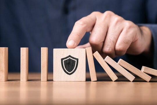 Wooden blocks arranged like domino with a shield symbol blocking the fall, representing protection, risk management, and prevention concept for business security, stability, and system resilience