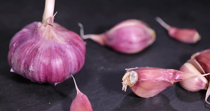 ripe purple garlic scattered on a table in the kitchen and cloves of crushed garlic , garlic spices lie on a black slate board in the kitchen over cooking
