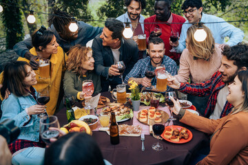 Multicultural friends dinner party celebrating together with food wine and drinks outdoors