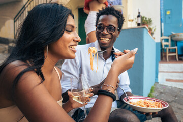 Multicultural friends eating pasta and drinking wine outdoors in Italy, summer vacation lifestyle