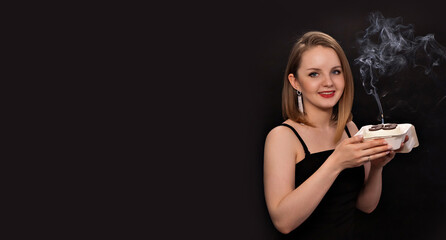 A woman in a black dress blows out a candle on a bento cake. Smoke on a black background. A girl's birthday, happiness, a gift. High quality photo