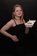 A woman in a black dress blows out a candle on a bento cake. Smoke on a black background. A girl's birthday, happiness, a gift. High quality photo