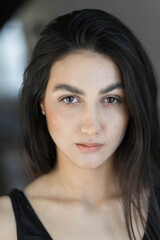 A woman with black hair wakes up in the morning in a white blanket and catches the rays of the sun. The portrait is creative, with brown eyes. High quality photo