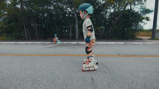 Toddler boy learns roller skating on the road in the park
