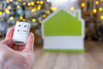 Security System Keychain in hand on background fairy lights Christmas tree and tiny house gift for New Year, Christmas. Home security, alarm system, SOS signal, protection from thieves