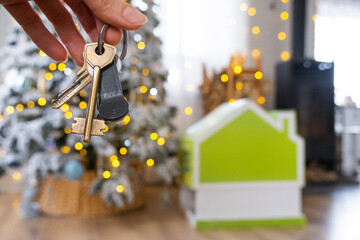 Keys in hand on background fairy lights Christmas tree and tiny house gift for New Year, Christmas. Building, design, project, moving, insurance, mortgage, rent and purchase real estate.