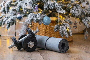 Sports equipment dumbbells, a fitness mat, and fitness bands lie under the Christmas tree at home as a gift for Christmas and New Year