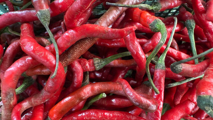 A close-up, overhead view of a pile of fresh, ripe red chili peppers with green stems.