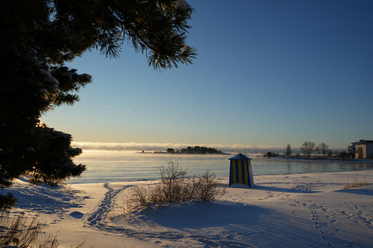 Winter beach scene with a small changing room and misty water at sunrise