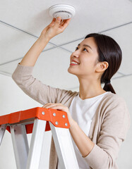 One happy Korean woman checking smoke detector at ceiling, safety concept.