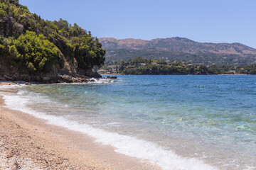 Obraz premium Empty pebble beach with turquoise water and distant village under clear sky