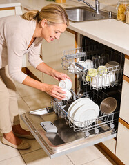 Woman putting dishware into dishwasher at home in the kitchen.