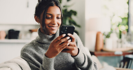 Fototapeta premium Phone, smile and woman on sofa in home with texting, social media or networking on mobile app. Happy, technology and female person with cellphone for chatting, contact or communication in living room