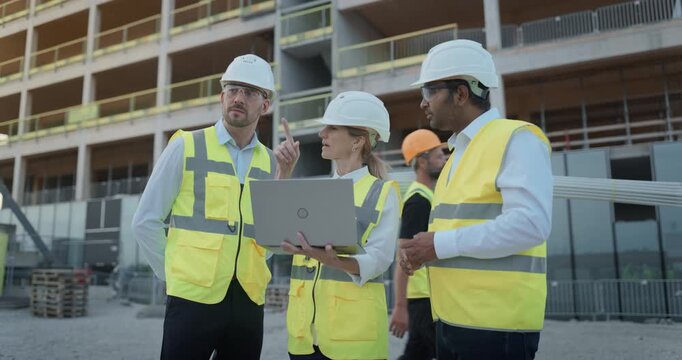 Two Male Construction Engineers on a Commercial Residential Building Site Use a Laptop to Review Structural Plans, Monitor Project Schedule, and Coordinate Real Estate Development Strategy