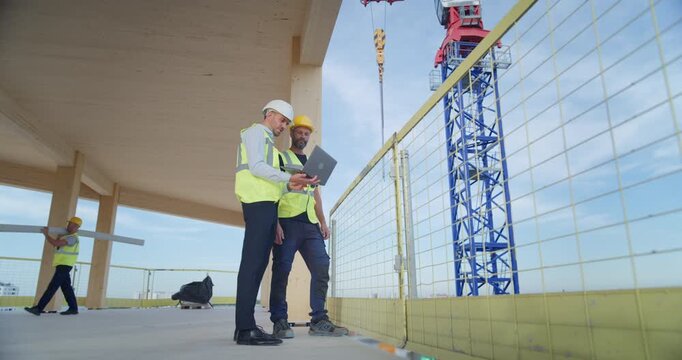 Male Construction Engineers Inside an Under Construction Commercial Residential Floor Use a Laptop to Track Structural Coordinate  Building Logistics, Plan of Real Estate Development 