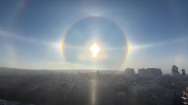Stunning solar halo phenomenon over a frosty winter city landscape. Bright sun dogs and a full circular halo create a breathtaking sky display.