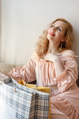 Obraz premium A blonde in a long pink dress poses by the window unwrapping gifts on International Women's Day.