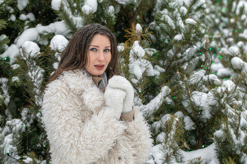 Winter portrait of a young beautiful brunette girl in an eco fur coat
