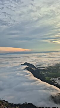 Amazing aerial view of thick white clouds rolling over a green mountain ridge at sunrise
