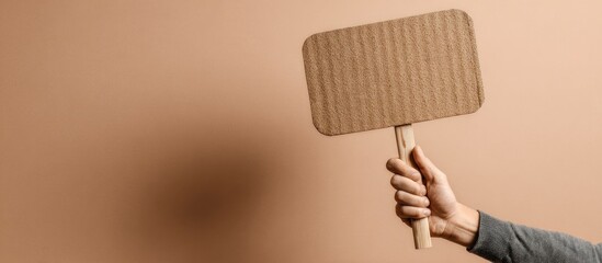 Hand holding a blank cardboard sign on a plain background.